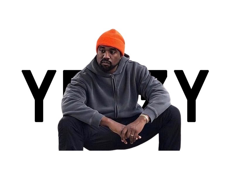 Kanye West Merch in bold black text behind a man in a gray hoodie and orange beanie, showcasing stylish streetwear apparel inspired by Kanye West.
